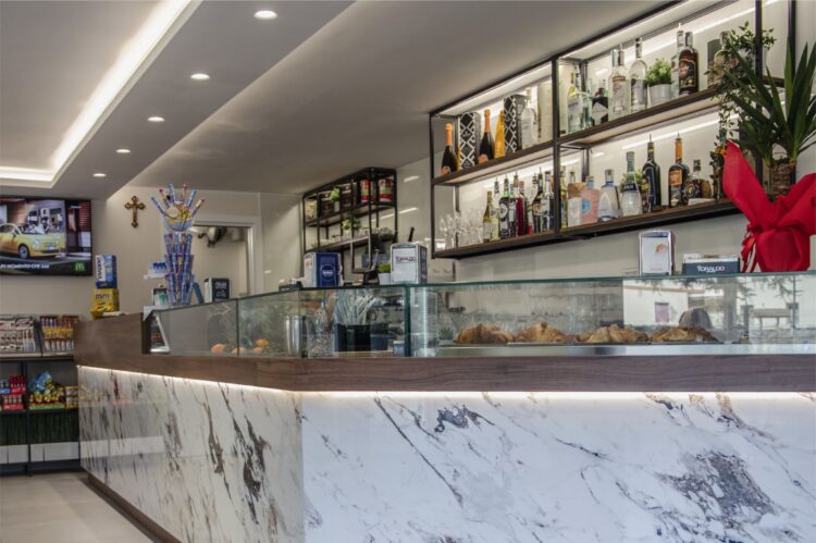 Interno di una caffetteria con bancone in marmo, scaffali di bottiglie e arredi moderni.
