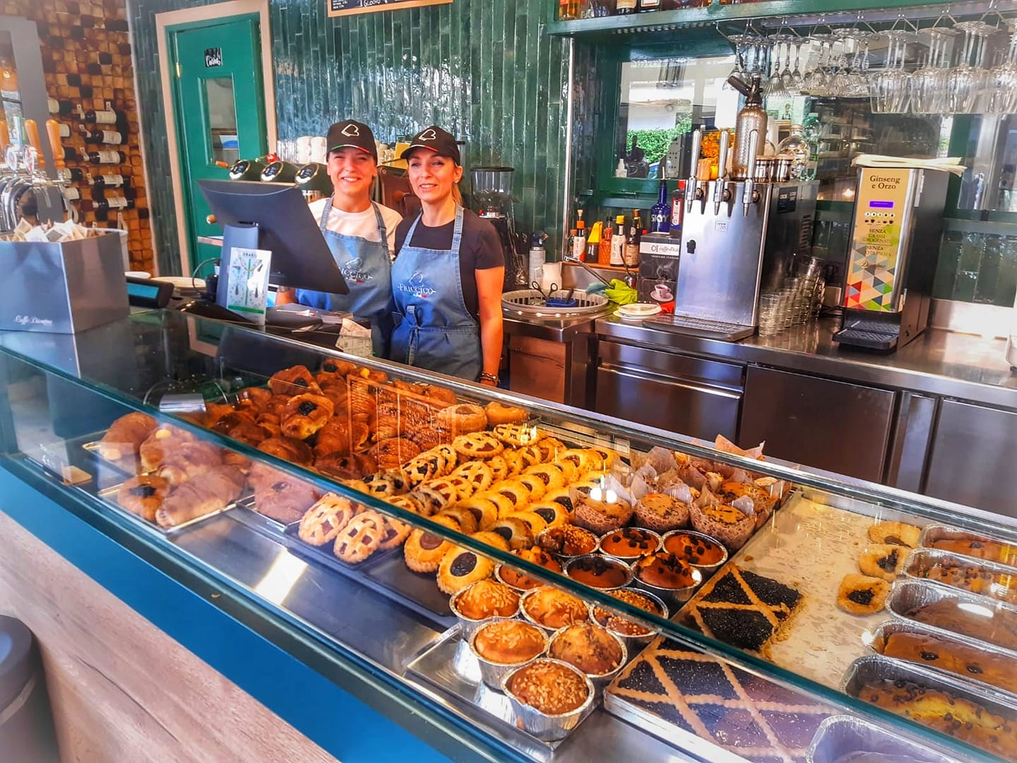 Interno di una pasticceria con bancone di dolci e personale sorridente.