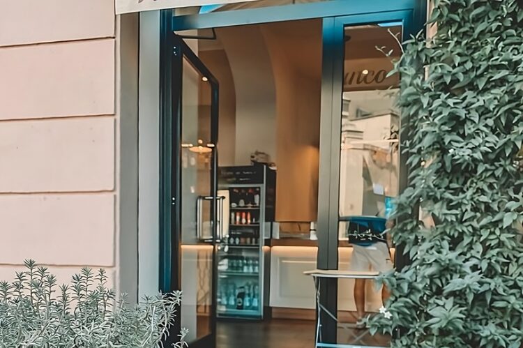Tavolino con cornetto e cappuccino, ingresso del locale e bancone laccato bianco crema e legno venato, Roma