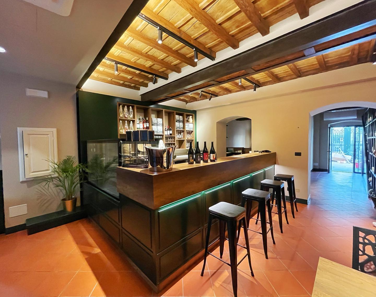 Interno di un bar con soffitto in legno, bancone in legno e marmo, bottiglie di vino esposte
