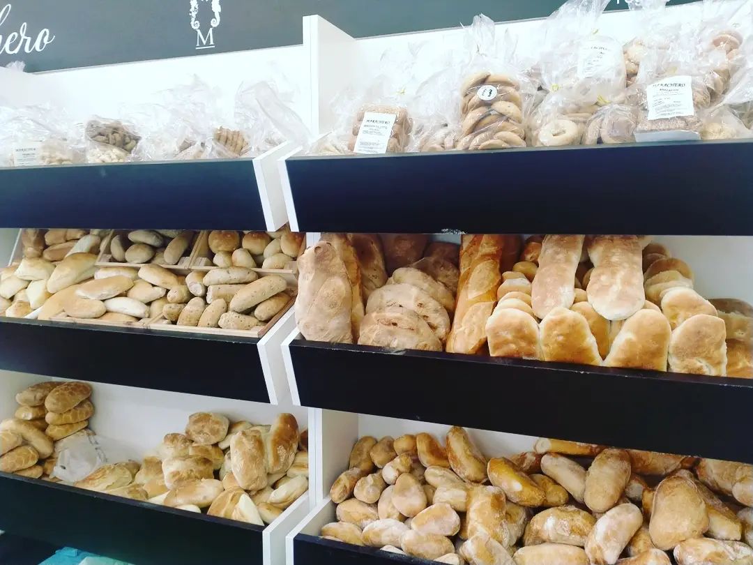 Scaffali di un panificio pieni di diversi tipi di pane fresco e biscotti confezionati. I pani sono di varie forme e dimensioni.
