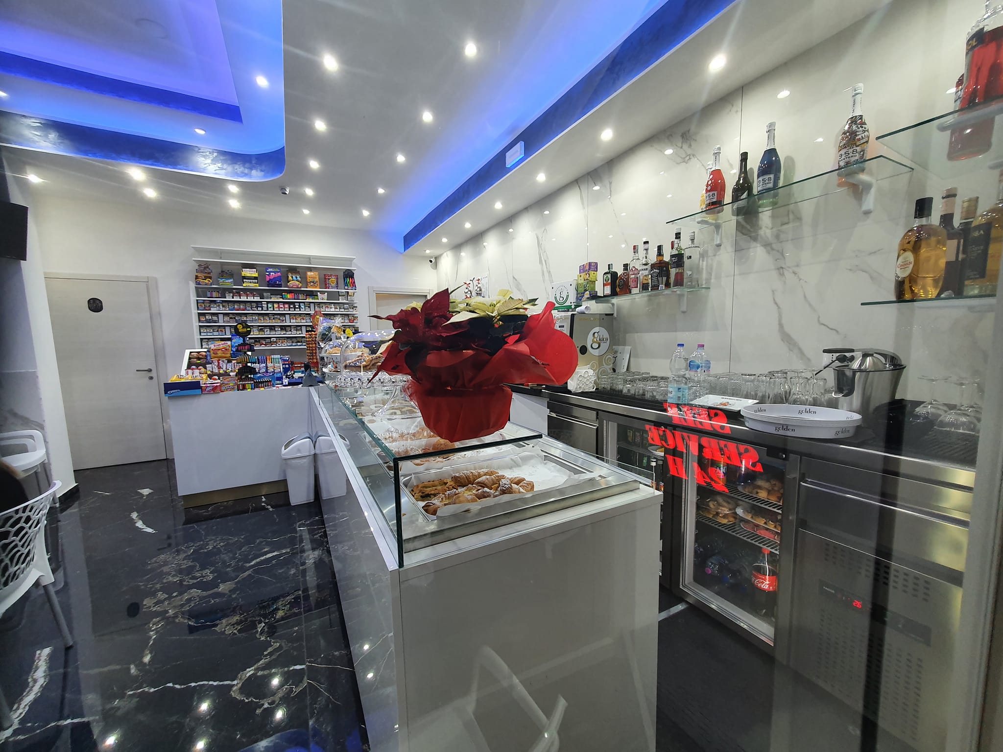 Interno del locale con vetrina pasticceria, scaffali con prodotti e illuminazione moderna