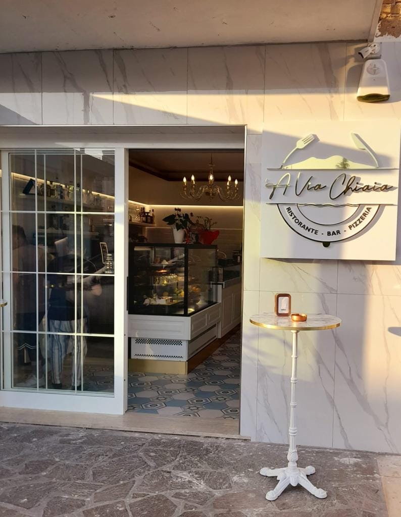 Vista dall'ingresso del locale con banco bar bianco stile provenzale, vetrina pasticceria da 150 cm e zoccolo dorato, realizzato da Agape Arredo Bar