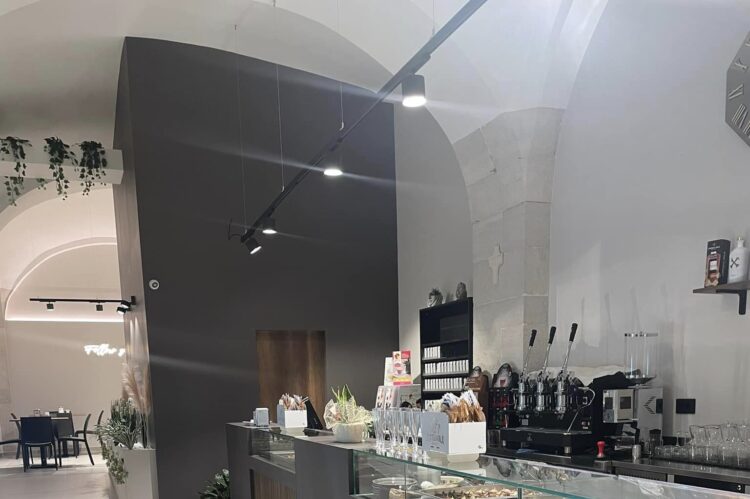 Interno di un locale moderno con bancone in legno e vetro, illuminazione a soffitto, e pavimento chiaro