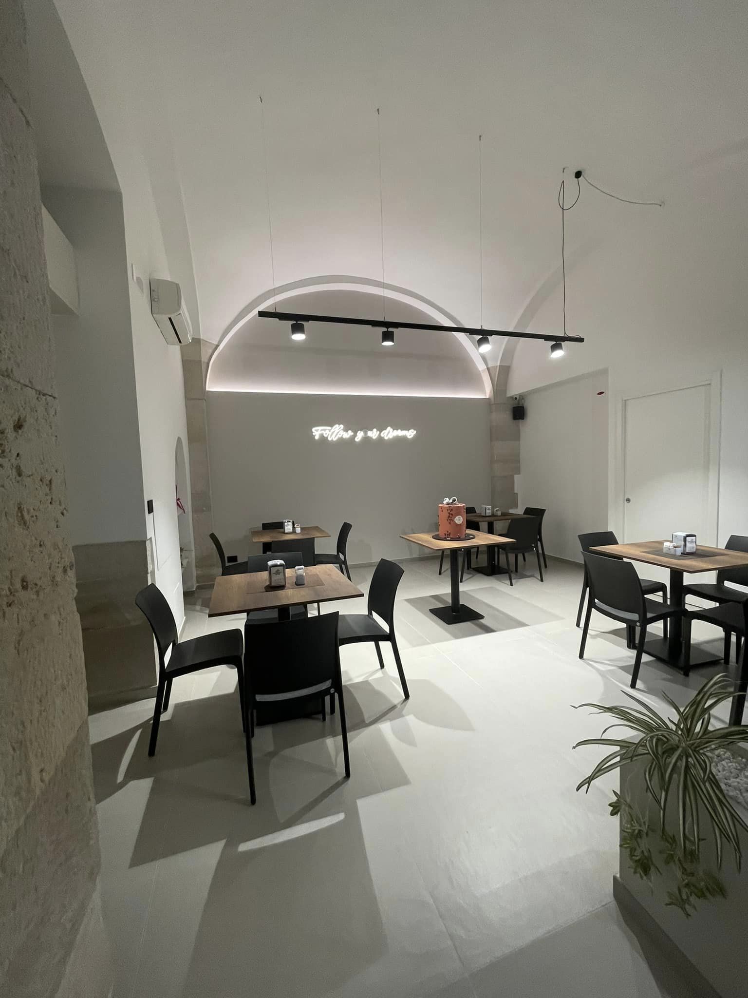 Interno di un locale con area seating, tavoli in legno, sedie nere, e insegna "Follow your dreams" sul muro