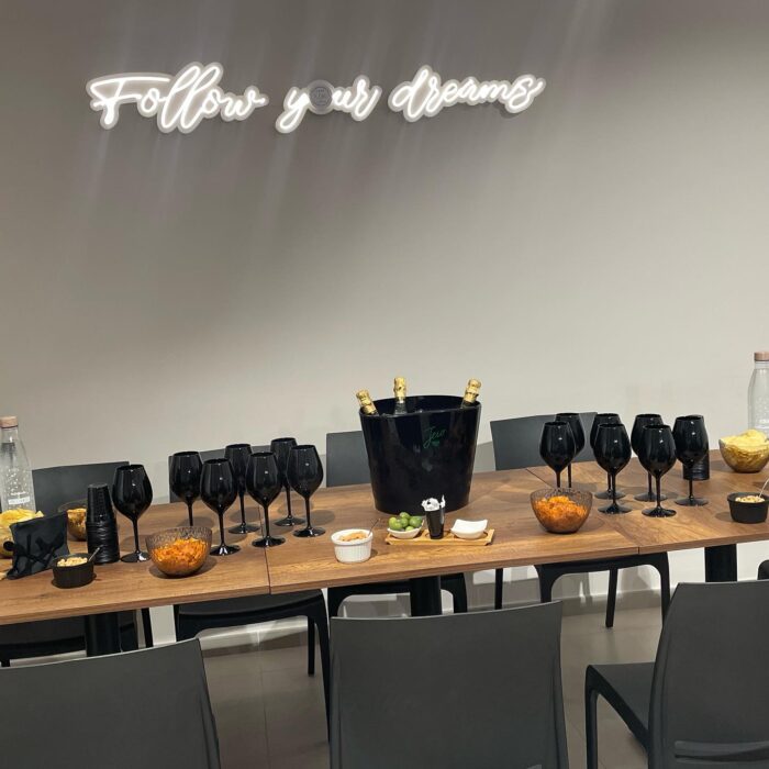 Tavolo con buffet, bicchieri neri, secchiello per champagne e insegna "Follow your dreams" sullo sfondo