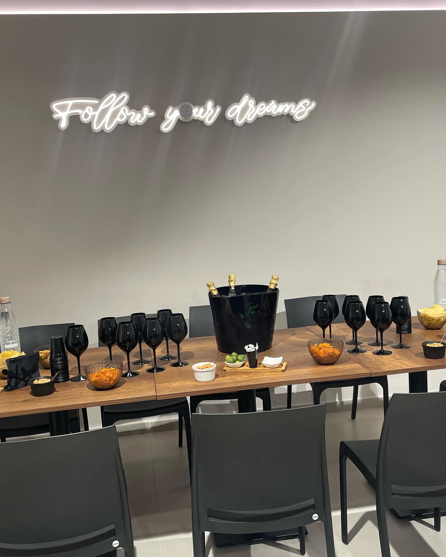 Tavolo con buffet, bicchieri neri, secchiello per champagne e insegna "Follow your dreams" sullo sfondo