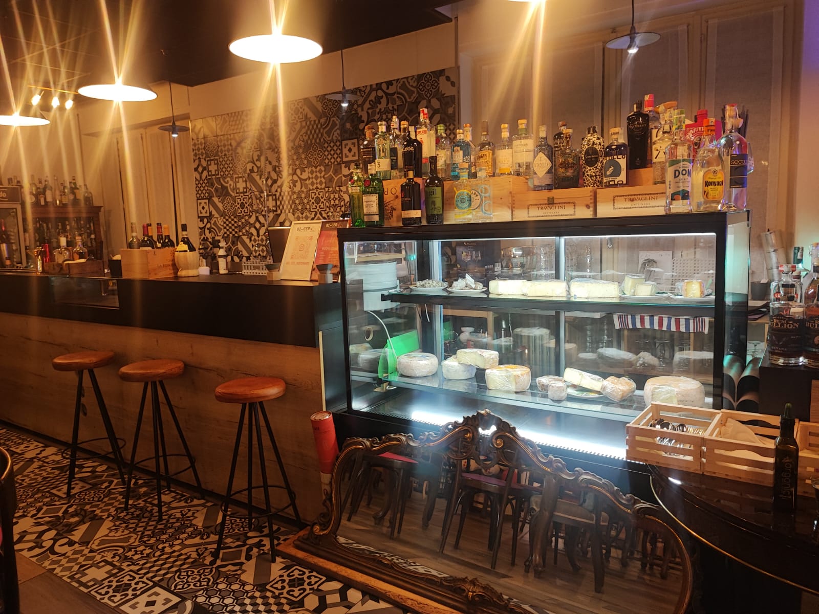 Bancone bar lato cliente con vetrina cubica da 150 cm con formaggi esposti, sgabelli e lampade sconce industrial, realizzato da Agape Arredo Bar