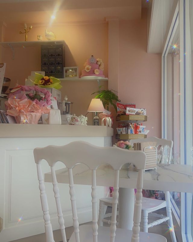 Interno di una caffetteria accogliente con sedie bianche, pareti rosa e decorazioni floreali sul bancone. Realizzato da Agape Arredo Bar.