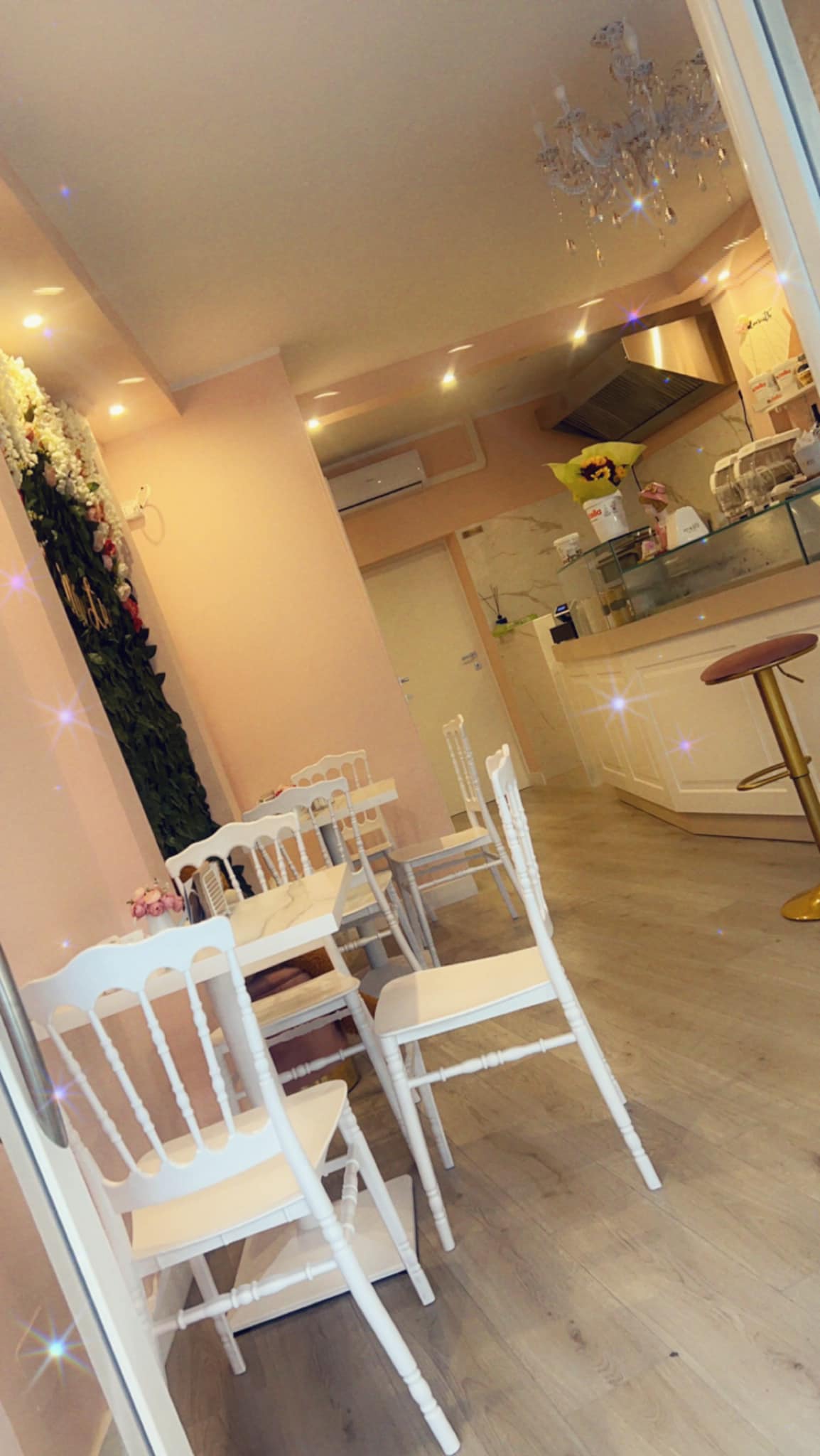 Interno di una caffetteria moderna con sedie bianche, pareti rosa e un bancone decorato con fiori. Realizzato da Agape Arredo Bar.