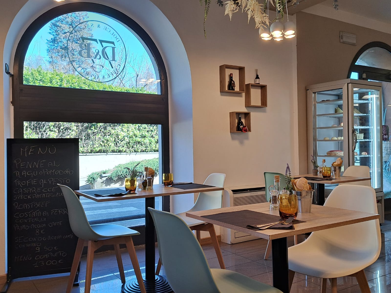 Interno di un bar ristorante moderno con sedie bianche e azzurre, tavoli apparecchiati e un menu scritto su una lavagna. Realizzato da Agape Arredo Bar