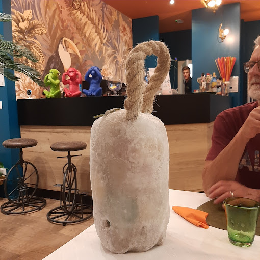 Dettaglio di un ristorante a tema tropicale con una decorazione originale sul tavolo, murale colorato e bancone bar sullo sfondo. Realizzato da Agape Arredo Bar
