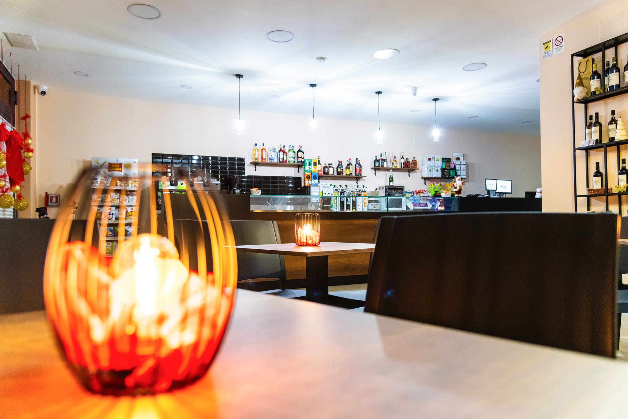 Interno di un bar moderno con illuminazione soffusa, bancone ben fornito e decorazioni eleganti, progettato da Agape Arredo Bar