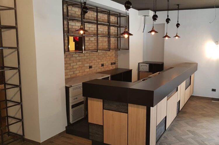 Cocktail bar stile industriale con frontale pannelli rettangolari finiture legno chiaro e scuro, lampadari industriali, realizzato da Agape Arredo Bar