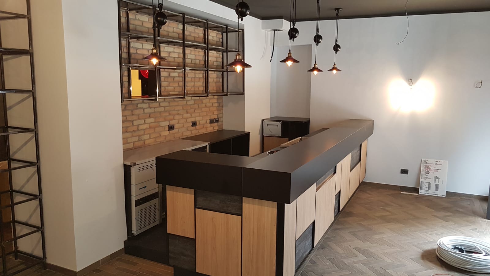 Cocktail bar stile industriale con frontale pannelli rettangolari finiture legno chiaro e scuro, lampadari industriali, realizzato da Agape Arredo Bar