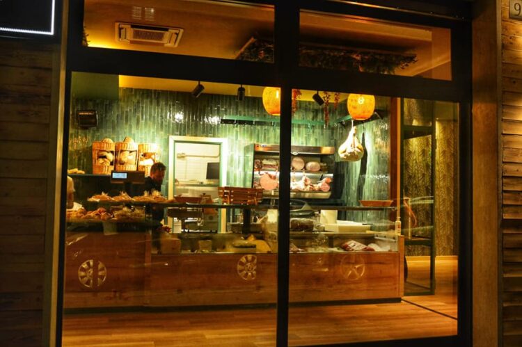 Vista esterna di un locale con vetrina illuminata, bancone con prodotti alimentari e decorazioni interne