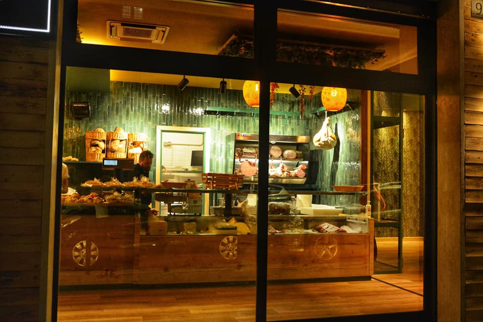 Vista esterna di un locale con vetrina illuminata, bancone con prodotti alimentari e decorazioni interne