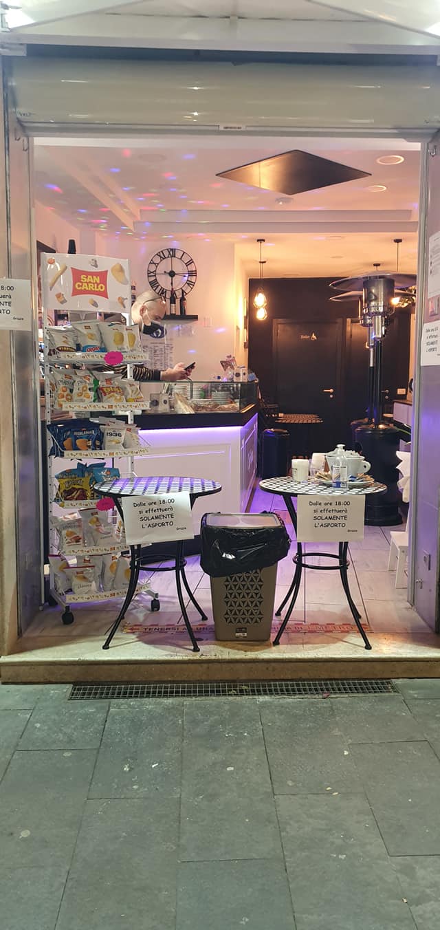 Ingresso di un bar moderno con illuminazione soffusa e area snack, progettato da Agape Arredo Bar