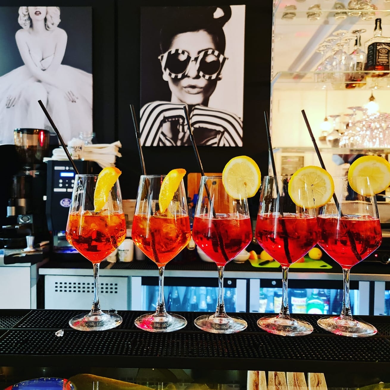 Cocktail colorati con arancia e limone su bancone di bar moderno, design by Agape Arredo Bar