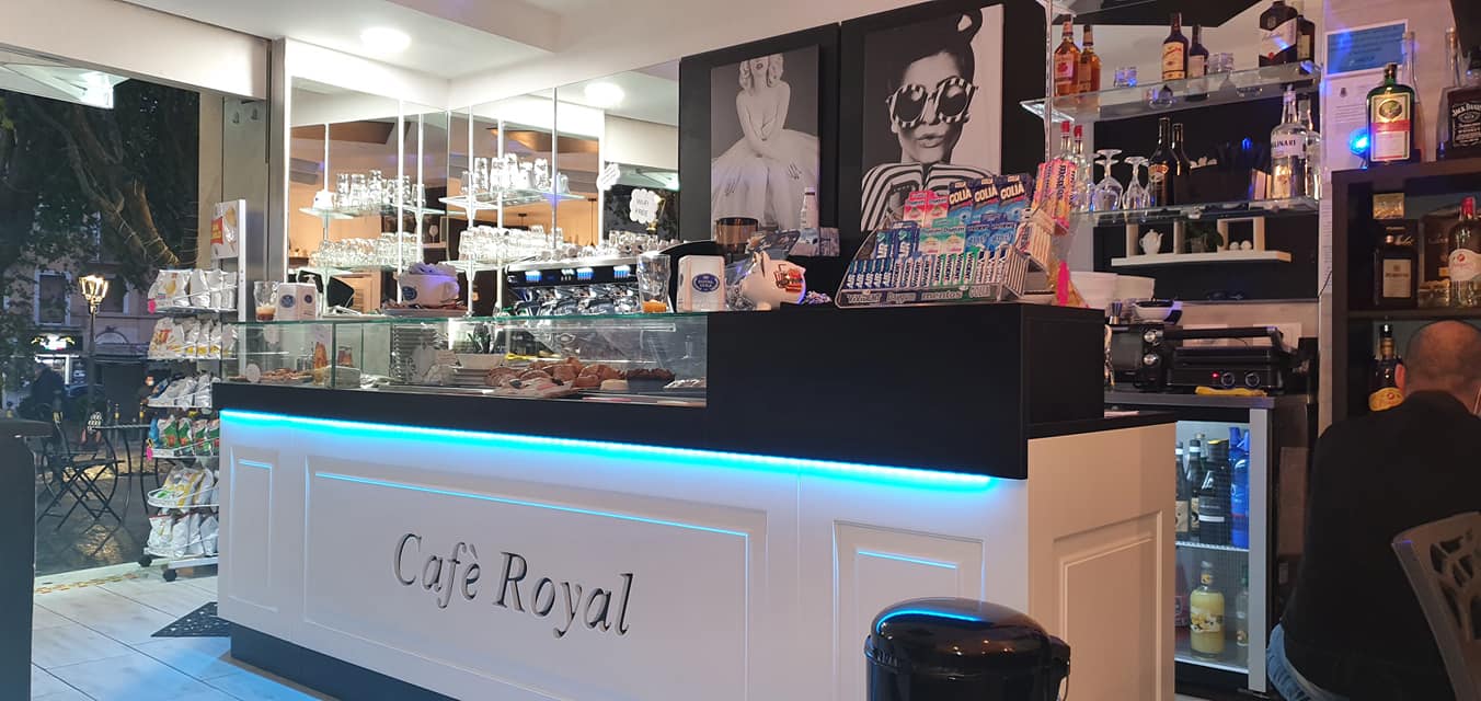 Bancone di un bar moderno con illuminazione LED blu e decorazioni chic, progettato da Agape Arredo Bar